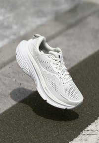 Baskets blanches avec une tige en mesh, détails texturés, col rembourré et une épaisse semelle en caoutchouc conçue pour le confort et la stabilité.