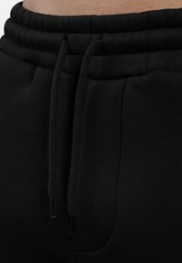 Sorte bomuldsjoggers med en elastisk talje og snoretræk samt sidelommer. Glat tekstur og minimalistisk design.