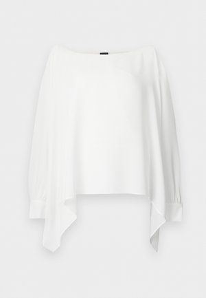 Blouse blanche à manches longues avec encolure bateau, ourlet asymétrique et larges poignets, présentée à plat sur un fond blanc.