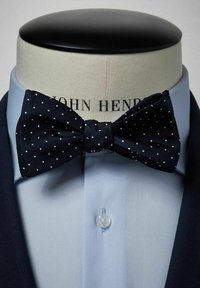 Marinblå prickig fluga i texturerad tyg, tillsammans med en ljusblå skjorta med knappar och spetsig krage.