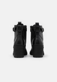 Czarne skórzane botki za kostkę z grubym obcasem, zamkami po bokach i paskami zdobionymi u góry. Teksturowane czarne gumowe podeszwy.