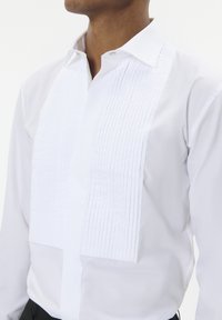 Valge särg, millel on volditud esipaneel, klassikaline krae ja voolav disain. Valmistatud siledast kangast, millel on nööbiga sulgemine.