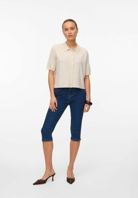 Gråbeige kortärmad skjorta med krage, kombinerad med mörka denimcaprijeans. Bruna klackmules och ett kraftigt armband kompletterar looken.