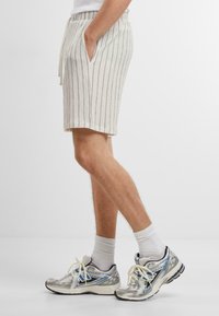 Pantalones cortos de color claro, con textura y rayas verticales, que cuentan con bolsillos laterales y una cintura con cordón, combinados con zapatillas de running reflectantes.