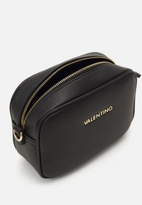 Svart lær kosmetikkveske med teksturert overflate, gullbeslag, dobbel glidelås, avrundede kanter og preget logo på forsiden.