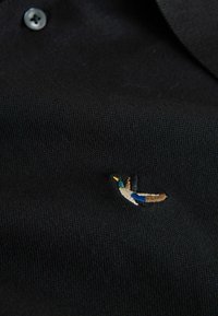 Tricou polo negru cu finisaj texturat, având un mic design brodat multicolor cu pasăre lângă tiv. Detaliu la guler cu nasturi.