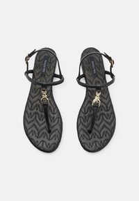 Svarte sandaler med en teksturert zigzag- såle, tynne stropper og et gullinsektcharms foran. Justerbar ankelstropp for passform.