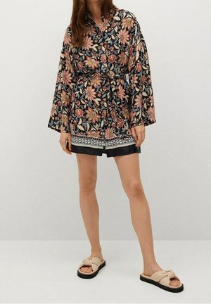 Schwarzer Kimono mit Blumenmuster, langen Ärmeln, einem Gürtel in der Taille und einem dekorativen Saum. Kombiniert mit beigen Rutsch-Sandalen.