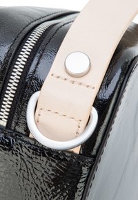 Angolo di borsa nera testurizzata con cerniera argento, tracolla in pelle beige fissata da rivetto metallico e attacco ad anello a D in argento.