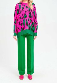Różowy i czarny sweter w panterkę w oversize'owym stylu, połączony z zielonymi spodniami o szerokich nogawkach oraz różowymi loafersami z złotymi akcentami. Miękka dzianinowa struktura.