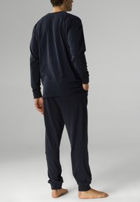 Navy blue zestaw koszulki z długim rękawem i spodniami wykonany z miękkiego materiału, o luźnym kroju i prążkowanych mankietach, model pokazany z tyłu, boso.