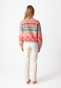 Färgglad mönstrad tröja med rosa, röd och blå geometriska mönster; ribbade ärmslut och nederkant; tillsammans med åtsittande vita byxor.