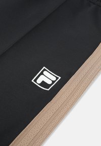 Zwarte stof met beige geribbelde rand en een klein wit geometrisch logo vlak bij de rand.