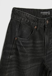 Czarne dżinsy o lekko wyblakłej fakturze, z zapięciem na guzik, pięcioma kieszeniami i metką oznaczoną "Stradivarius."