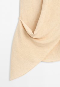 Beige stof met een puntige zoom detail bevestigd met een kleine knoop, met textuur en gedrapeerde plooien op een witte achtergrond.