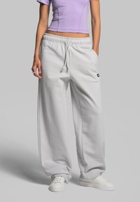 Helle graue, weit geschnittene Sweatpants aus weichem Stoff, mit einem elastischen Bund und Kordelzug sowie einem kleinen schwarzen Logo an der Seite.
