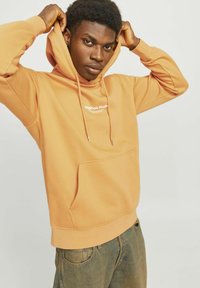 Oranje hoodie met capuchon, met een voorzak en trekkoorden. Witte tekst met "Originals Studio" op de borst. Zachte katoenen stof.