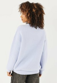 Maglione oversize azzurro chiaro realizzato in morbido pile testurizzato, con spalle scese e polsini a coste. Il design sul retro presenta una vestibilità ampia.