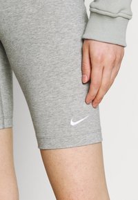 Pantalones cortos de ciclismo de mezcla de algodón gris con un ajuste ceñido, que presentan un logo blanco de Nike en la parte inferior de la pierna izquierda y un detalle de cinturilla acanalada.