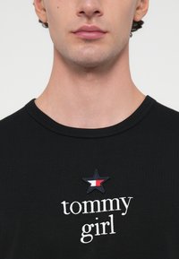 Černé bavlněné tričko s kulatým výstřihem, vyšitým nápisem "tommy girl" a designem hvězdy v námořnické modré, bílé a červené barvě.
