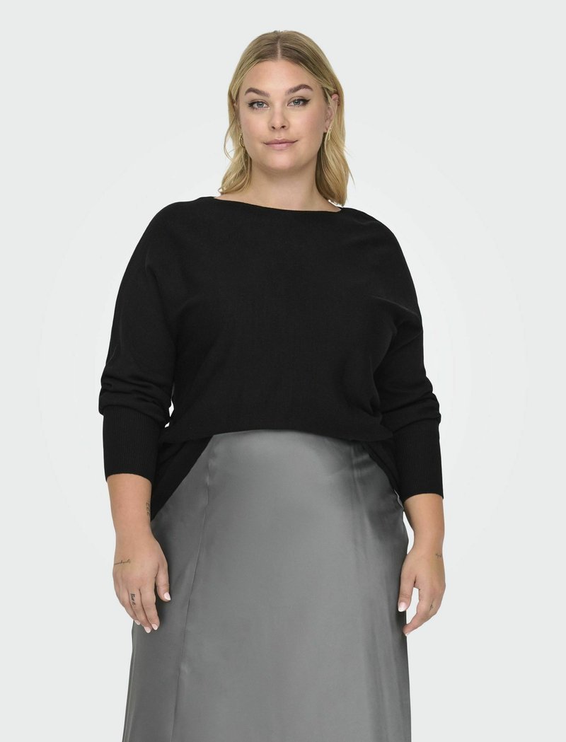 Melna adīta džemperis ar plašu laivu formas kaklu un garām piedurknēm, kombinēts ar spīdīgu pelēku satīna svārku. Gluda tekstūra, brīvs piegriezums.