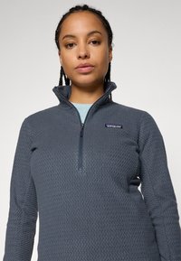 Grijze fleece pullover met een gestructureerd oppervlak, 1/4 rits kraag en Patagonia-logo op de linkerborst. Lange mouwen met een aansluitend ontwerp.