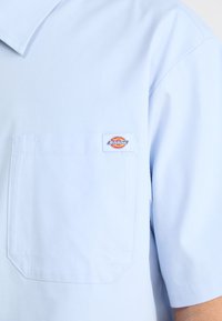 Svetlo modra kratka srajca iz gladkega blaga z žepom na prsih in prišito Dickies oznako. Klasična zasnova ovratnika.