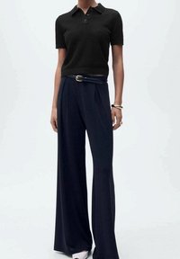 Polo noir côtelé avec col, associé à un pantalon large bleu marine, doté d'une taille ceinturée et d'une texture de tissu lisse et fluide.