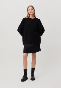 Black oversized knit sweater with ribbed hem, paired with a black fitted skirt and knee-high lace-up leather boots. Smooth texture overall.