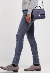 Liten marinblå handväska med strukturerad yta, fyrkantig form och silverlås. Bärs med grå tröja och åtsittande blå jeans, kombinerat med grå skor.