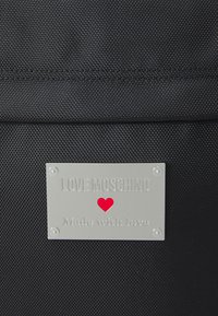 Black textured fabric bag with a silver metal plate inscribed “LOVE MOSCHINO” and a red heart, featuring subtle stitching details.