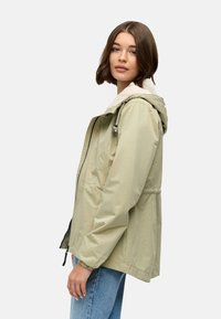 Lys olivengrønn jakke laget av lett stoff, med hette med faux pelsfôr, elastiske mansjetter og snor i livet.