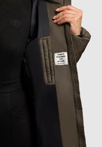 Olīvzaļa, polsterēta jakas iekšpuse ar kviltotu tekstūru. Iespējo etiķete ar uzrakstu "Siltas apskāvienas, kas izgatavotas no auduma." Melna auduma otrā pusē.