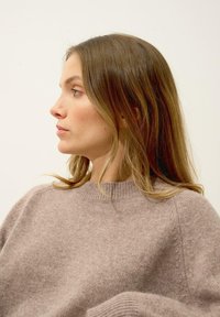 Jasnobrązowy sweter dzianinowy z okrągłym dekoltem i prążkowanymi mankietami. Miękka tekstura, lekko luźny krój, podkreślający swobodną sylwetkę.