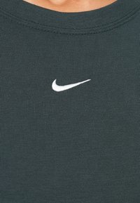 Žalia raižinė medvilnės marškinėliai su apvalia iškirpte, turintys mažą baltą Nike logotipą viršutiniame kairiajame kampe.