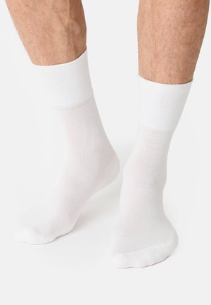 White cotton socks with a smooth texture, ribbed cuffs, and a simple design. They cover the ankle and show minimal detailing.