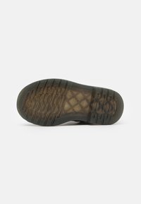 Suela de zapato con una superficie de goma texturizada, que presenta un patrón geométrico y estrías para mejorar la tracción. El color es predominantemente oscuro con acentos translúcidos.