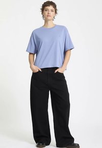Lichtpaars cropped t-shirt met korte mouwen, gecombineerd met losse zwarte broek met wijde pijpen. De outfit heeft een ontspannen pasvorm en zachte stof.
