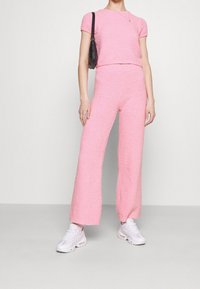 Różowy, dzianinowy zestaw składający się z bluzki z krótkim rękawem i spodni z szerokimi nogawkami, połączony z białymi sneakersami i małą czarną torebką.