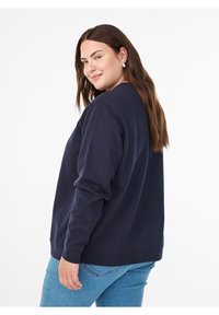 Tumesinine pusa, millel on pikad varrukad ja ümar kaelus, iseloomustab lõdvestunud istuvus ja sile tekstuur. Kandmiseks koos helesiniste teksadega.