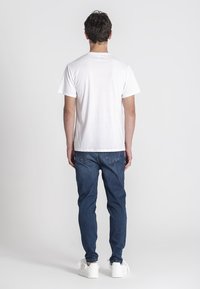 Biała bawełniana koszulka o klasycznym kroju, zestawiona z ciemnymi dżinsami. Model ma na sobie białe trampki. Minimalistyczny design, jednolite kolory.