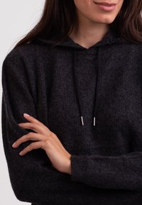 Felpa con cappuccio di maglia grigia scura con superficie testurizzata, dotata di cappuccio con cordino e accessori in metallo argentato. Vestibilità ampia con maniche larghe.