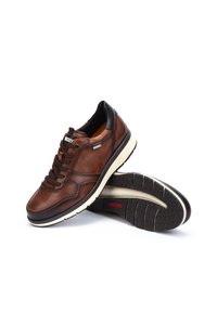 Zapatillas de cuero marrón con una superficie texturizada, acentos en el talón negros y suela de goma blanca. Presentan cordones y un logo en el lateral.