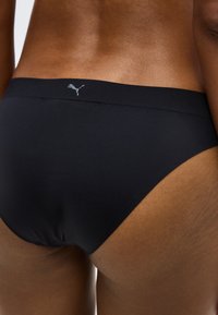 Κοντινό πλάνο ενός ατόμου που φοράει μαύρα αόρατα μπριφ με μικρό λογότυπο Puma στη μέση, δείχνοντας τον κάτω μέρος της πλάτης και το πάνω μέρος των μηρών.