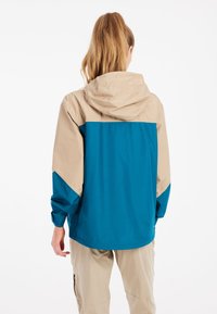 Mikina s kapucňou, ktorá má modrú spodnú časť a rukávy, s béžovou hornou časťou. Vyrobená z hladkého, ľahkého materiálu.