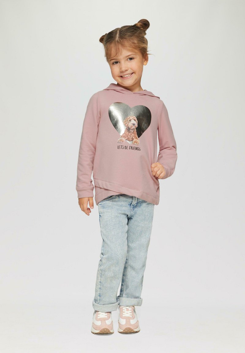 Roze hoodie met een hartvormige zilveren print waarop een hond staat en de tekst "Laten we vrienden zijn," gecombineerd met lichtblauwe jeans en roze sneakers.
