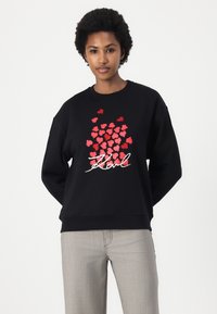 Sweatshirt preto com um aglomerado de corações vermelhos e texto em letras brancas. Manga longa, corte descontraído e punhos e bainha canelados.