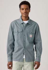 Blauw-wit gestreepte overhemd met knopen, voorzien van twee borstzakken, een klein logo-patch en een kraaghals. Gemaakt van katoen met een gestructureerde afwerking.