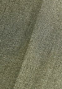 Zielony lniany materiał o lekko teksturowanej powierzchni. Tkanina jest lekka i tkana, ukazując subtelne różnice w kolorze i splocie.