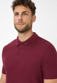 Polo a maniche corte color bordeaux con tessuto a trama, colletto a punta e chiusura a tre bottoni.